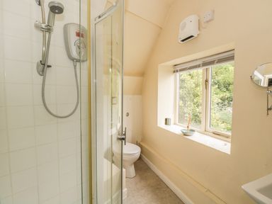 A bathroom with a shower cabin a toilet a window with a blind and a small wall-mounted mirror at Pembridge Cottage in Welsh Newton