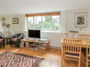 A living room with two leather chairs a TV on a wooden stand and a dining table with chairs at Pembridge Cottage in Welsh Newton
