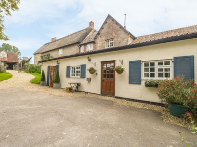 A cottage exterior with blue shuttered windows wooden doors flower baskets and a gravel path at Colly Cottage in Dottery