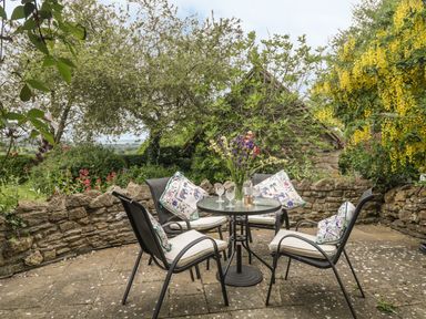 An outdoor patio with a round table four chairs and a stone wall garden at Colly Cottage in Dottery