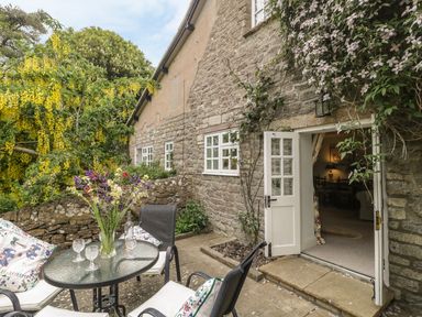 An outdoor patio area with a round glass table chairs and flowers next to a stone wall cottage at Colly Cottage in Dottery