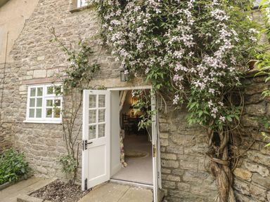 A stone exterior wall with an open white door and flowering vines at Colly Cottage in Dottery