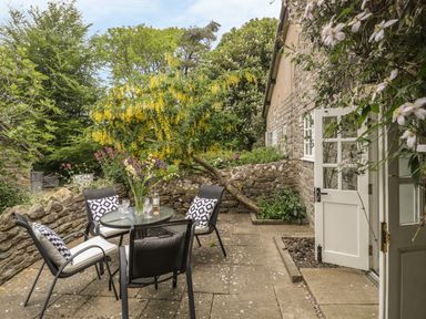 A stone patio with a glass table and four chairs with cushions outside a stone house at Colly Cottage in Dottery