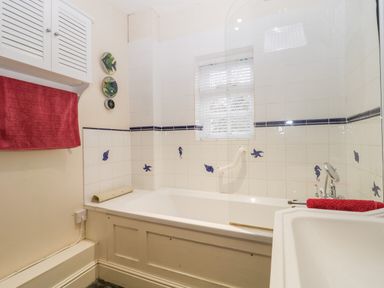 A bathroom with a bathtub framed by white tiles decorated with blue sea creatures a sink and red towels at Colly Cottage in Dottery