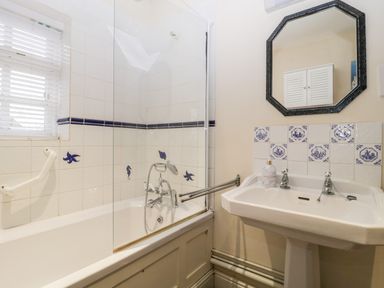 A bathroom with a bathtub, handheld shower, sink with separate taps, and a mirror at Colly Cottage Dottery