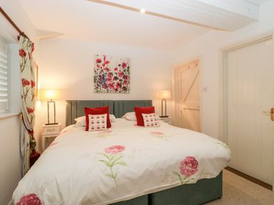 A bedroom with a large bed two bedside tables lamps floral curtains and floral artwork at Colly Cottage in Dottery