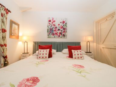 A bedroom with a double bed with floral bedding two bedside tables with lamps and floral curtains at Colly Cottage in Dottery