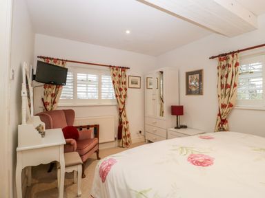 A bedroom with a bed a wardrobe a dressing table an armchair and windows with floral curtains at Colly Cottage in Dottery
