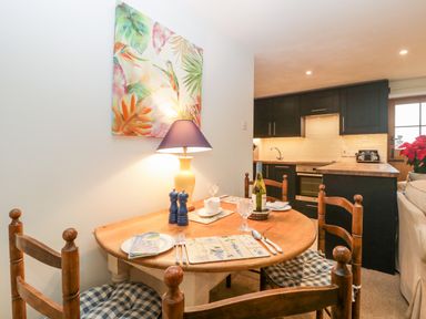 A dining area with a wooden table set for four and a kitchen with dark cabinets in the background at Colly Cottage in Dottery
