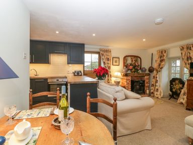 A kitchen and living area with wooden dining table kitchen cabinets and a sofa near a fireplace at Colly Cottage in Dottery