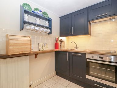 A kitchen with dark cabinets a wooden countertop an oven a sink and a wall shelf with mugs at Colly Cottage in Dottery