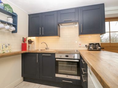 A kitchen with dark cabinets a stainless steel oven and sink wooden countertops and a toaster on the counter at Colly Cottage in Dottery