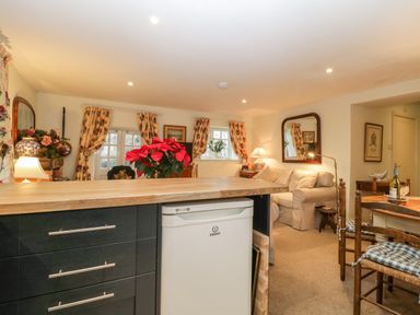 A living room and kitchen area with a wooden countertop refrigerator and dining table with chairs at Colly Cottage in Dottery