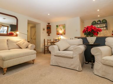 A living room with beige sofas a small wooden table with a red flowerpot a dining table with wooden chairs and a kitchen counter in the background at Colly Cottage in Dottery