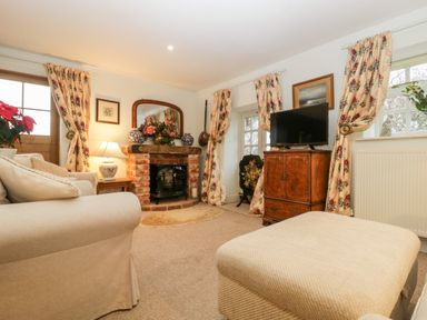 A living room with a beige sofa a fireplace a TV on a wooden cabinet and floral curtains at Colly Cottage in Dottery