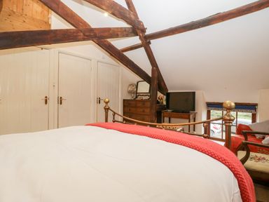 A bedroom with wooden beams a bed with white and red bedding a dresser a TV on a table and a window at Colly Cottage in Dottery