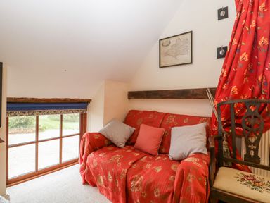 A room with a red floral sofa covered with cushions next to a window with a blue blind and a wooden chair with a floral seat at Colly Cottage in Dottery