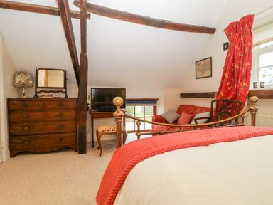 A bedroom with a brass bed a wooden chest of drawers a TV on a small table and a red sofa at Colly Cottage in Dottery