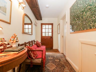 A hallway with a wooden bench with red cushions a wooden side table a wall mirror a map and a wooden door at Colly Cottage in Dottery