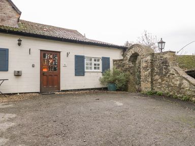 An outdoor area with a white building featuring a wooden door and blue shutters next to a stone archway at Colly Cottage in Dottery