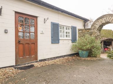 An entrance door and window with shutters on a white wall near a stone arch and potted plant at Colly Cottage in Dottery