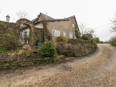 A stone house with white-framed windows near a gravel driveway and a stone wall with an arched iron gate at Colly Cottage in Dottery