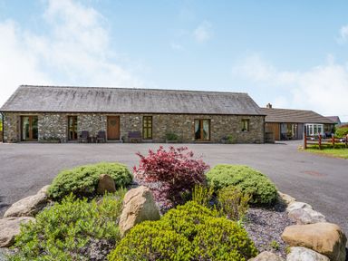 A stone building with wooden doors and windows surrounded by shrubs and rocks at Ysgubor Hir in Pontarddulais near Swansea