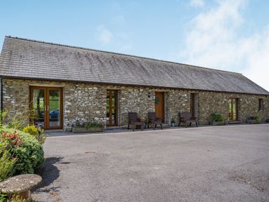 Stone building with wooden doors and windows two brown chairs and benches outside at Ysgubor Hir in Pontarddulais near Swansea
