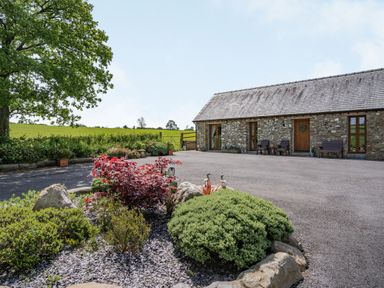 A stone building with wooden doors and windows and garden shrubs in the foreground at Ysgubor Hir in Pontarddulais near Swansea