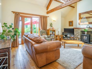 A living room with leather sofas wooden coffee table and a television near a stone fireplace at Ysgubor Hir in Pontarddulais near Swansea