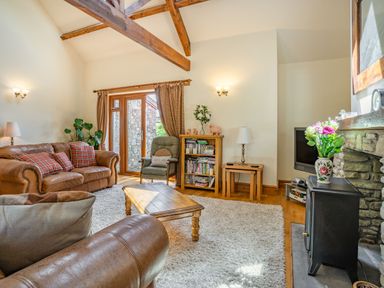 A living room with leather sofas a wooden coffee table and a television by a stone fireplace at Ysgubor Hir in Pontarddulais near Swansea