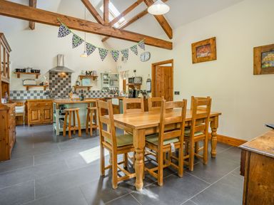 A kitchen dining area with a wooden dining table and chairs wooden beams and kitchen island at Ysgubor Hir in Pontarddulais near Swansea