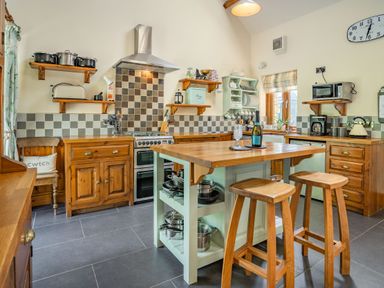 A kitchen with wooden cabinets a central island with stools and cooking utensils at Ysgubor Hir in Pontarddulais near Swansea
