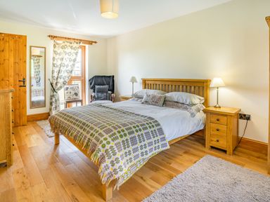 A bedroom with a wooden bed and bedside tables a large mirror chair and windows with patterned curtains at Ysgubor Hir Pontarddulais near Swansea