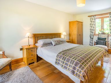 A bedroom with a double bed bedside tables lamps wooden wardrobe and window with curtains at Ysgubor Hir in Pontarddulais near Swansea