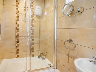 A shower area with sliding glass doors a wall-mounted electric shower a small basket and a wall-mounted mirror and towel ring at Ysgubor Hir in Pontarddulais near Swansea