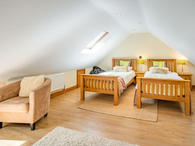 A bedroom with two wooden single beds a beige armchair and a skylight window at Ysgubor Hir in Pontarddulais near Swansea