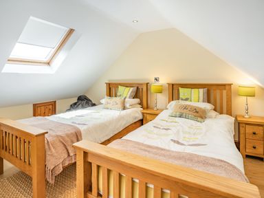 A bedroom with two wooden beds bedside tables and lamps under a skylight window at Ysgubor Hir in Pontarddulais near Swansea