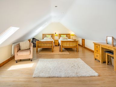 A bedroom with two single wooden beds a beige armchair a wooden dresser and two rugs at Ysgubor Hir in Pontarddulais near Swansea