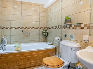 A bathroom with a bathtub wooden toilet seat a sink and tiled walls at Ysgubor Hir in Pontarddulais near Swansea