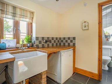 A kitchen sink with wooden countertop and small fridge under counter near a window and door to a bathroom at Ysgubor Hir in Pontarddulais near Swansea
