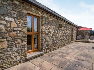 An outdoor patio area with stone walls wooden framed window and outdoor seating with red umbrella at Ysgubor Hir in Pontarddulais near Swansea