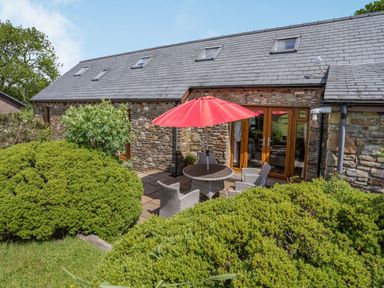 A stone house with a slate roof and a patio with a round table and four chairs under a red umbrella at Ysgubor Hir in Pontarddulais near Swansea
