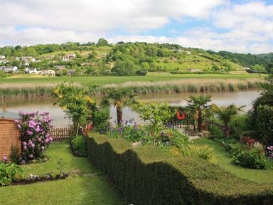 A garden with hedges and flowers overlooking a river with houses and trees on the opposite hillside at Tuckermarsh Quay River Cottage 2 Bere Alston near Tavistock