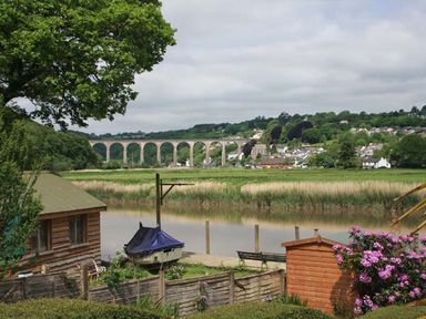 A riverside scene with a wooden shed boat covered with a blue tarp and a stone viaduct in the background at Tuckermarsh Quay River Cottage 2 Bere Alston near Tavistock