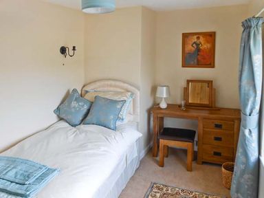A bedroom with a single bed with blue pillows and folded towels next to a wooden desk with a mirror and lamp at Tuckermarsh Quay River Cottage 2 Bere Alston near Tavistock
