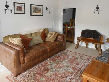 A living room with a leather sofa and wooden chair with cushions and a patterned rug at Tuckermarsh Quay River Cottage 2 Bere Alston near Tavistock