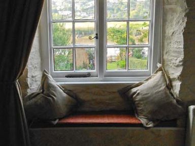 A window seat with cushions and a view of a garden through a window at Tuckermarsh Quay River Cottage 2 Bere Alston near Tavistock