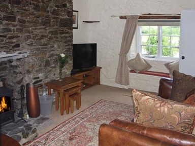 A living room with a stone fireplace a television a window seat with cushions and wooden furniture at Tuckermarsh Quay River Cottage 2 Bere Alston near Tavistock