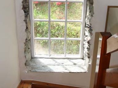 A stone framed window with white grid panes overlooking a garden with red flowers and greenery at Tuckermarsh Quay River Cottage 2 Bere Alston near Tavistock